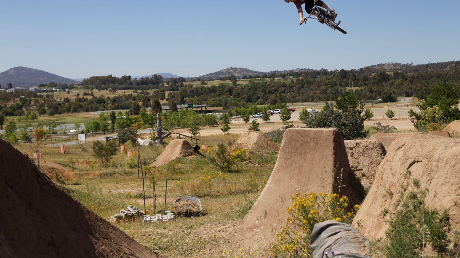mike hucker clark doing a 360 on a bmx bike off a big dirt step down jump with a blue sky background with mountains in the distance