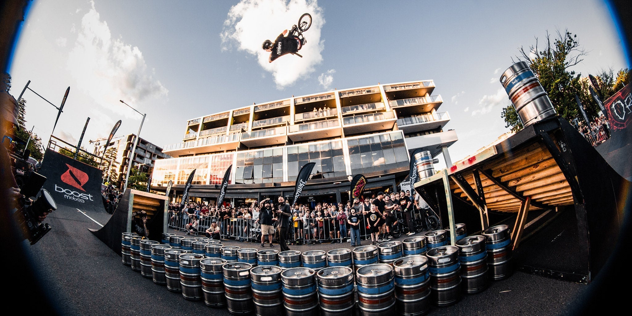 act jam 2025 braddon bmx event josh dove backflipping over lots of kegs with apartment building in backkground