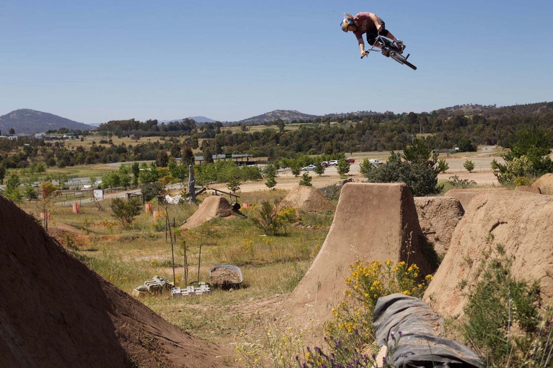 mike hucker clark doing a 360 on a bmx bike off a big dirt step down jump with a blue sky background with mountains in the distance